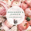 A hand-tied bouquet of soft pink and blush ranunculus flowers filling the frame, with a large translucent white oval overlay in the center reading “DESIGNER’S CHOICE” and “HAND-TIED BOUQUET,” plus an ornate monogram logo.