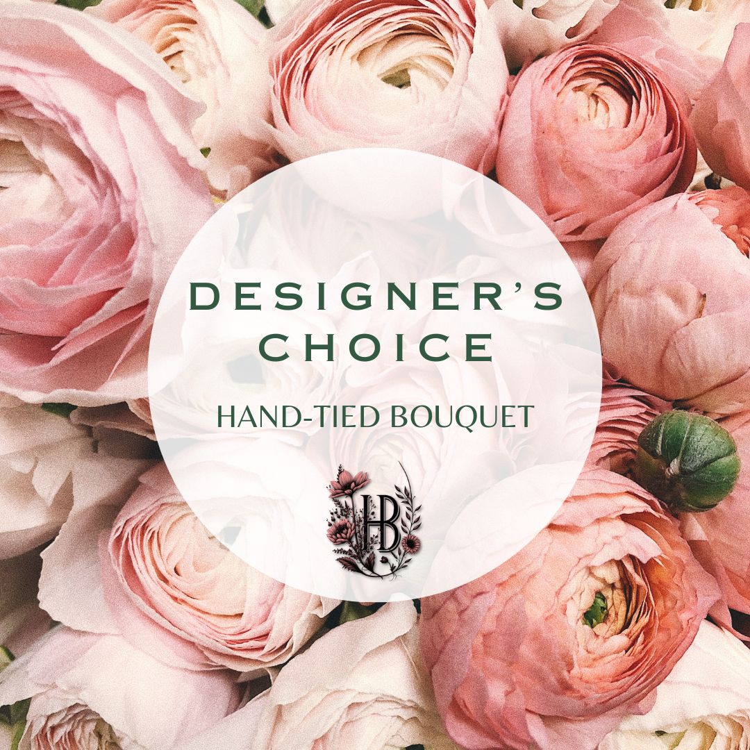 A hand-tied bouquet of soft pink and blush ranunculus flowers filling the frame, with a large translucent white oval overlay in the center reading “DESIGNER’S CHOICE” and “HAND-TIED BOUQUET,” plus an ornate monogram logo.