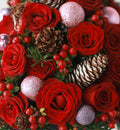 A close-up of a festive holiday floral arrangement featuring vibrant red roses, natural pinecones, red berries, and glittery silver ornaments.