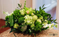 A lush green floral arrangement featuring hydrangeas, roses, orchids, anthurium and various green foliage, designed by Harmonic Blooms in Glastonbury, CT and displayed on a granite countertop with a softly blurred indoor background.