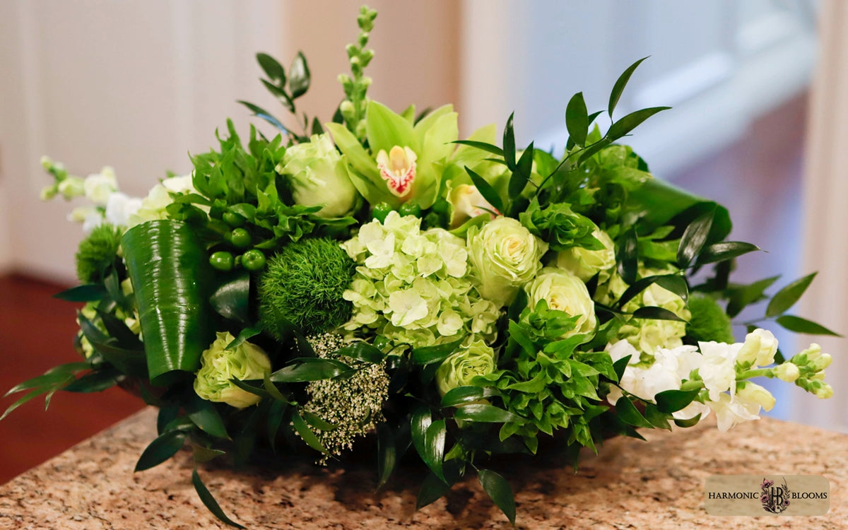 A lush green floral arrangement featuring hydrangeas, roses, orchids, anthurium and various green foliage, designed by Harmonic Blooms in Glastonbury, CT and displayed on a granite countertop with a softly blurred indoor background.
